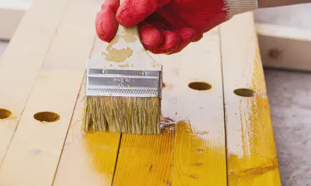 a builder applies yellow paint with a brush to wood